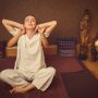 Thai massage stretch. Relaxed young woman is sitting on floor in lotus position. Masseuse is touching her arms